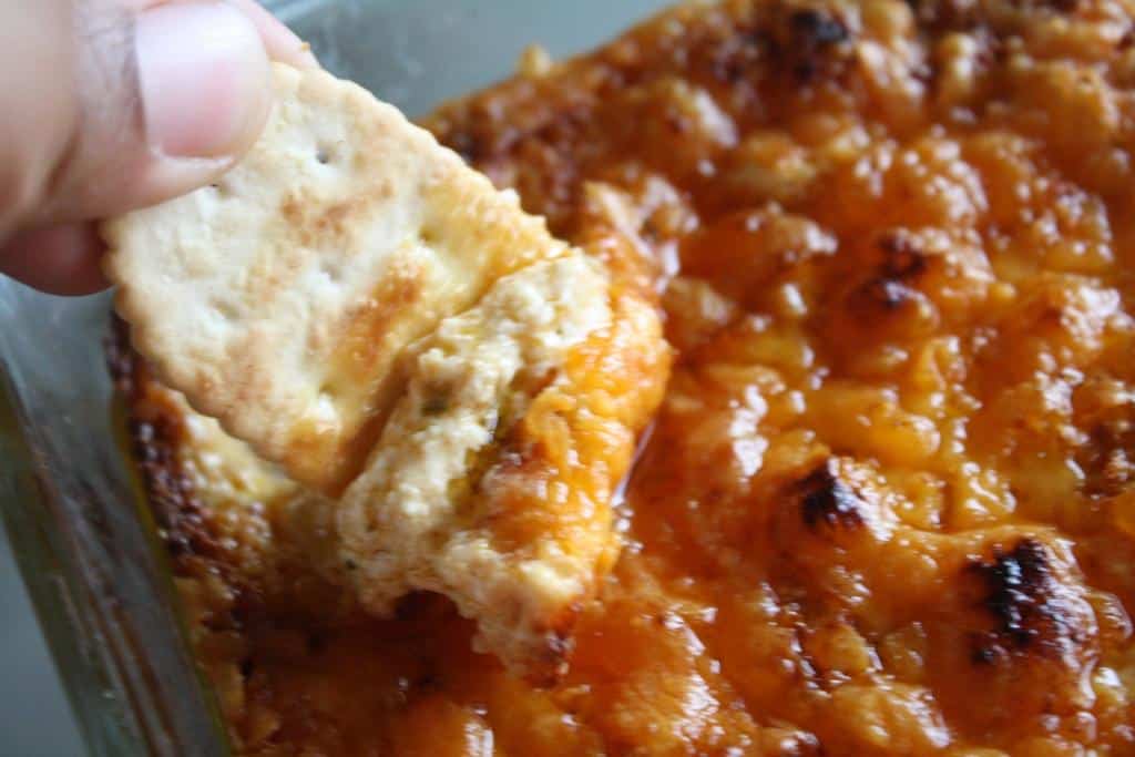 Hand dipping cracker into buffalo dip.