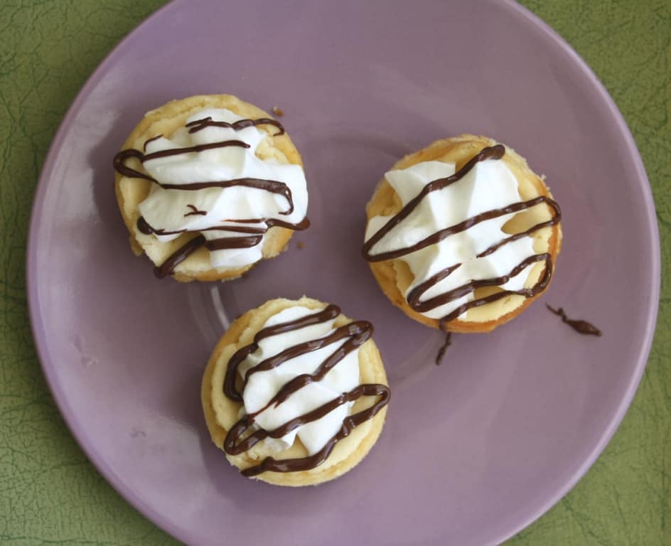 Overhead shot of three mini cheesecakes on a purple plate.