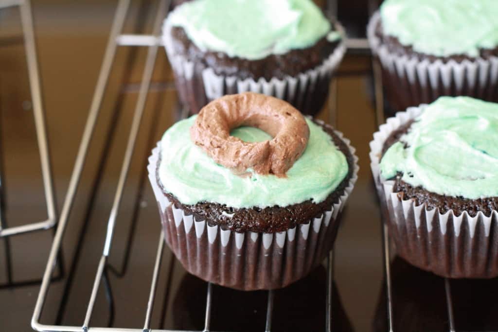 A ring of brown frosting piped onto a cupcake lightly frosted with teal frosting. 