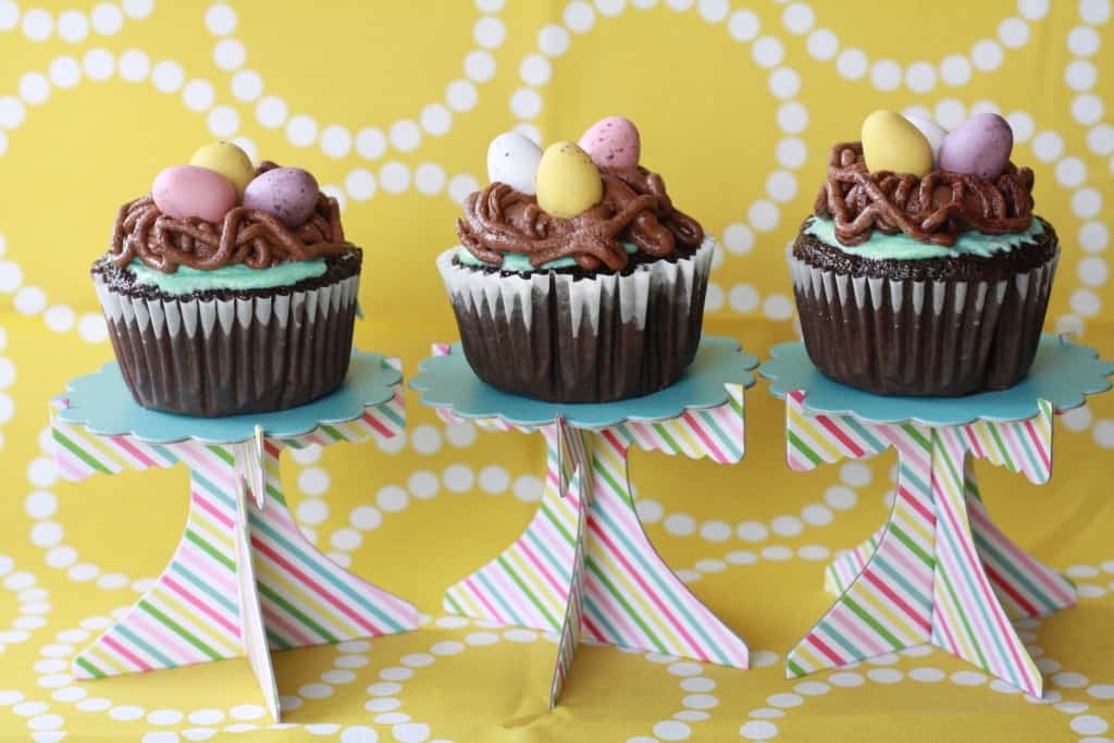 Three bird's nest cupcakes on mini cake stands.