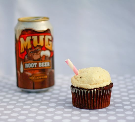 An iced cupcake next to a can of root beer. 