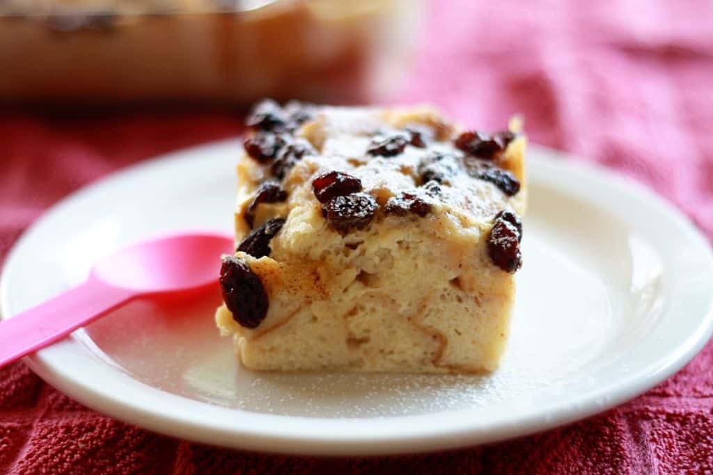 Side shot of a square of dessert with raisins on a white plate.