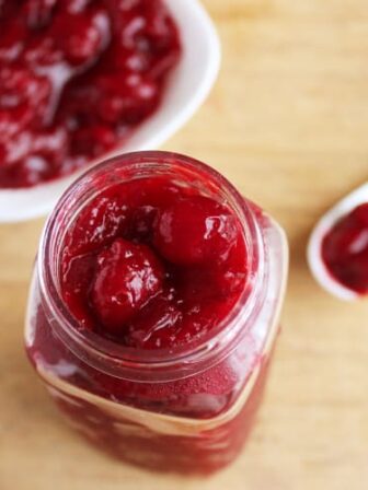 Cranberry sauce in a glass jar with a spoon next to it.