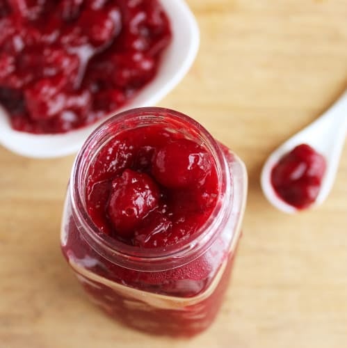 Top down view of cranberry orange sauce in a glass jar, with a spoon on the side. 