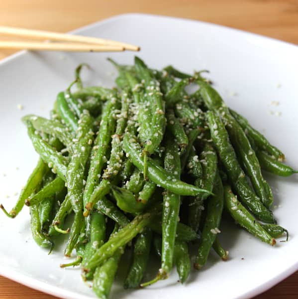 A pile of garlic parmesan sesame stir fry green beans on a square white plate. 