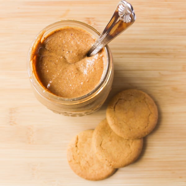 Top down shot of cookie butter in a glass jar with three cookies on the side. 
