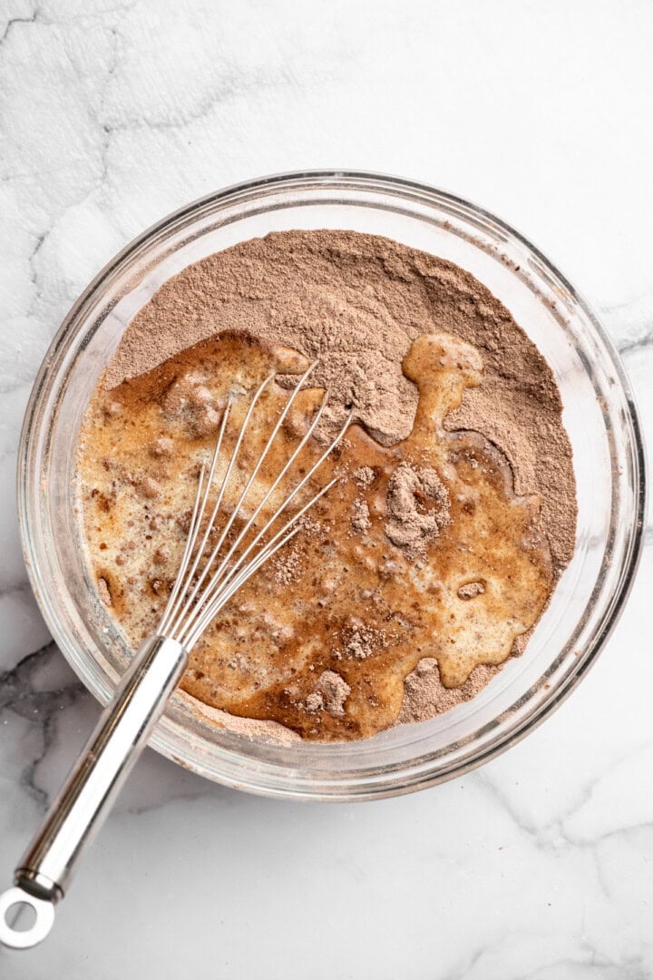 Dry ingredients added to wet ingredients in bowl with whisk.
