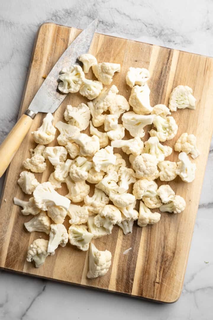 These cheesy Buffalo cauliflower wings are made with a spicy batter and a panko coating for a double-crispy vegan game day snack! Cauliflower florets on cutting board with knife.