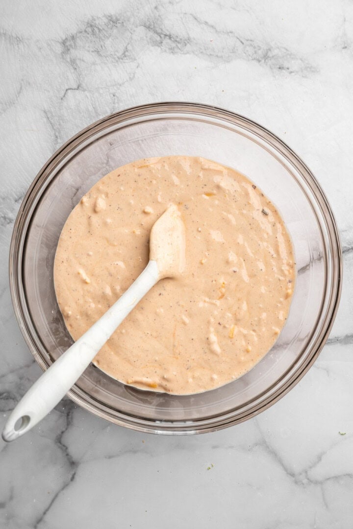These cheesy Buffalo cauliflower wings are made with a spicy batter and a panko coating for a double-crispy vegan game day snack! Bowl of batter with rubber spatula.