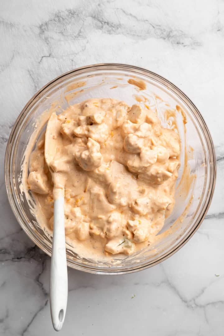 These cheesy Buffalo cauliflower wings are made with a spicy batter and a panko coating for a double-crispy vegan game day snack! Stirring cauliflower in bowl with batter.