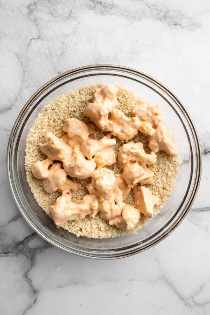 These cheesy Buffalo cauliflower wings are made with a spicy batter and a panko coating for a double-crispy vegan game day snack! Battered cauliflower wings added to bowl of panko.