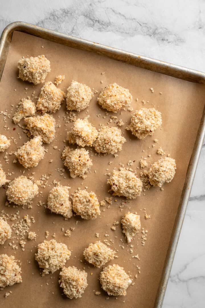 These cheesy Buffalo cauliflower wings are made with a spicy batter and a panko coating for a double-crispy vegan game day snack! Buffalo cauliflower wings on pan before baking.