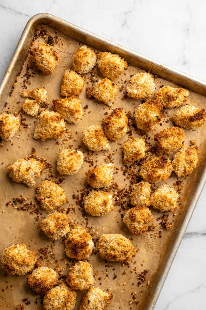 These cheesy Buffalo cauliflower wings are made with a spicy batter and a panko coating for a double-crispy vegan game day snack! Baked cheesy buffalo cauliflower wings on sheet pan.