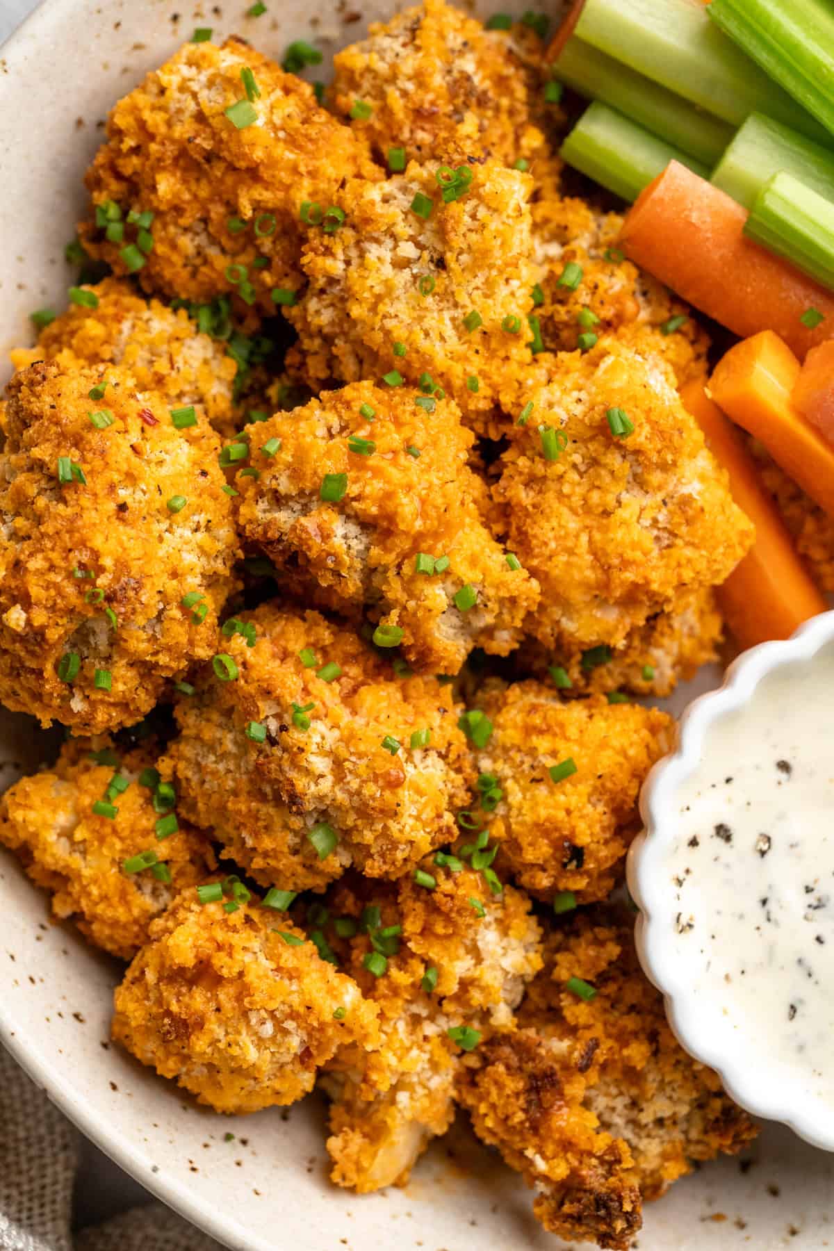 These cheesy Buffalo cauliflower wings are made with a spicy batter and a panko coating for a double-crispy vegan game day snack! Platter of cheesy Buffalo cauliflower wings with celery, carrots, and ranch.