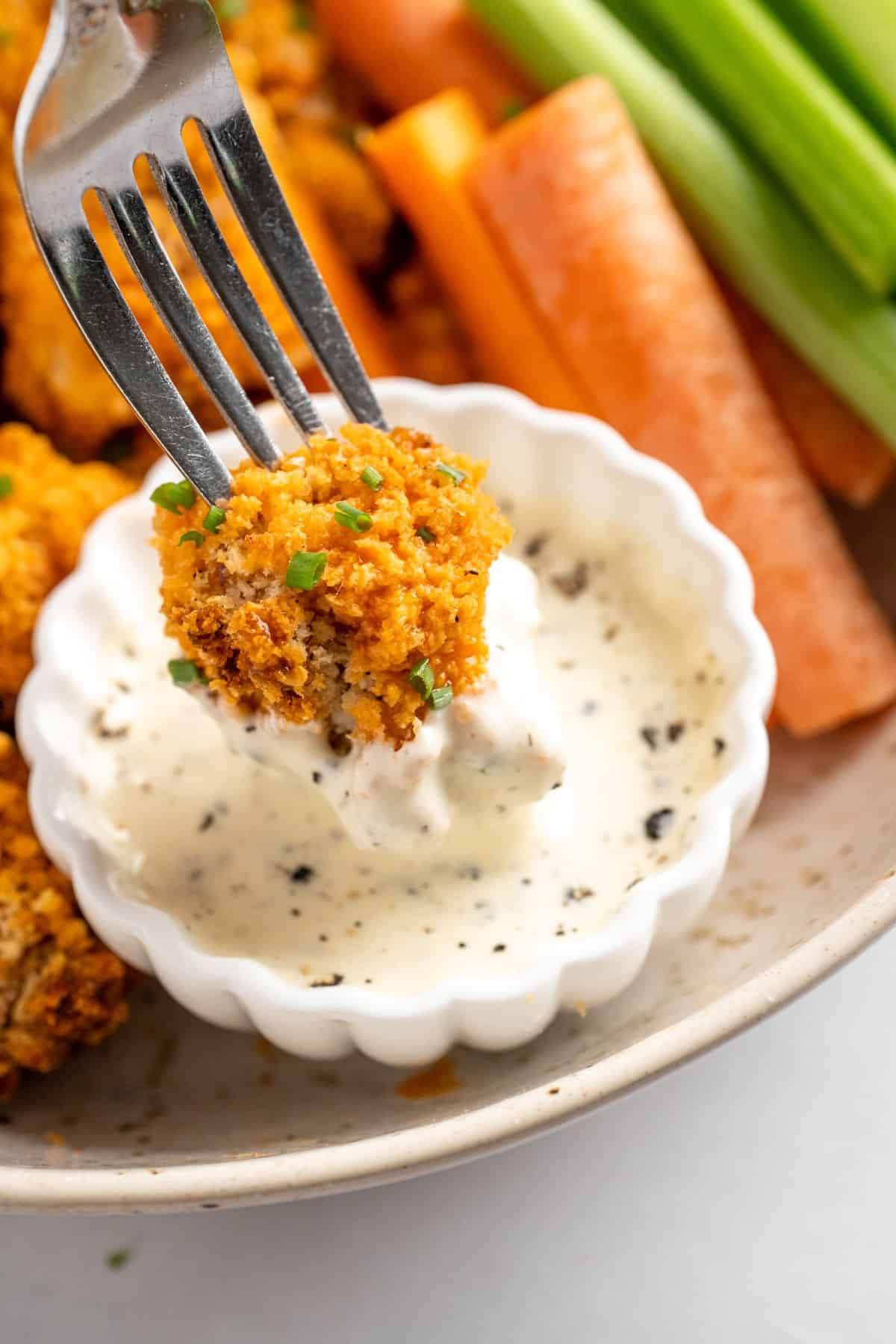 These cheesy Buffalo cauliflower wings are made with a spicy batter and a panko coating for a double-crispy vegan game day snack! Fork dipping cheesy buffalo cauliflower wing into vegan ranch.