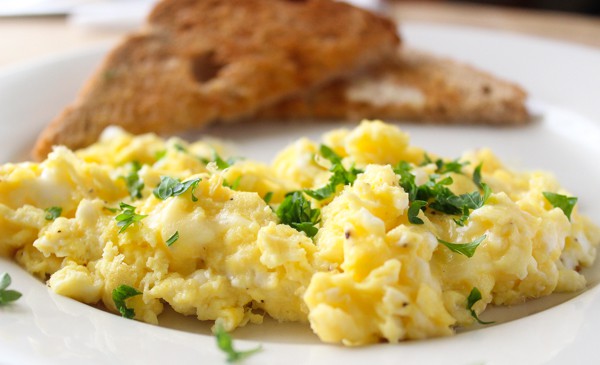 Scrambled egss on a plate with brown toast.