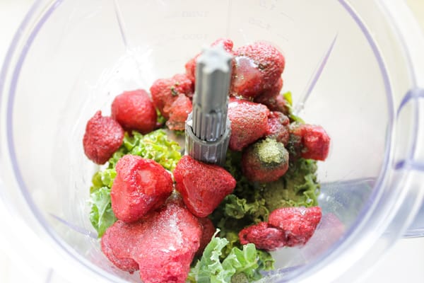 Overhead view of kale and frozen strawberries in blender