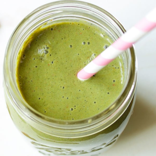 Overhead view of strawberry kale smoothie in mason jar with pink and white striped straw