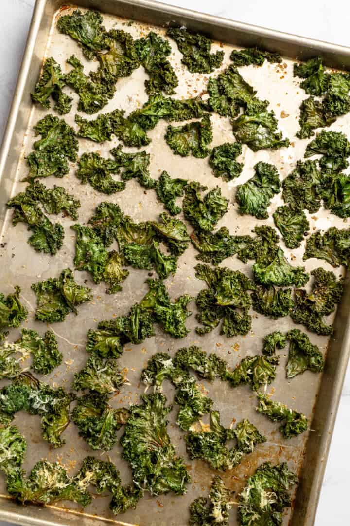 Whether you season them with sea salt, black pepper, or vegan Parmesan, these crispy baked kale chips are an easy snack ready in minutes! Sheet pan with crispy kale chips.