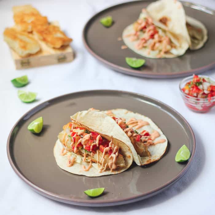 Fish Tacos on two grey plates with lime wedges.