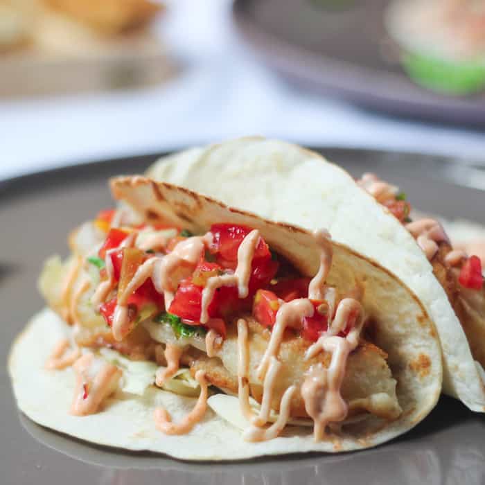 Close up of fish tacos with sriracha mayo on a grey plate.