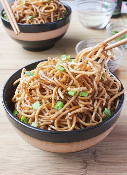 Chopsticks holding Sesame Noodles with Honey Ginger Sauce over black and brown bowl.