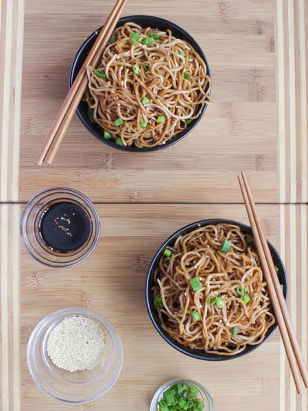 Overhead shot of Sesame Noodles with Honey Ginger Sauce in 2 separate bowls with say sauce and sesame seeds in small bowls beside them .