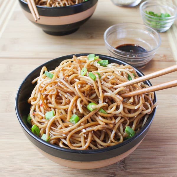 Sesame Noodles with Honey Ginger Sauce in a bowl with chopsticks in them and soy sauce on the side. 