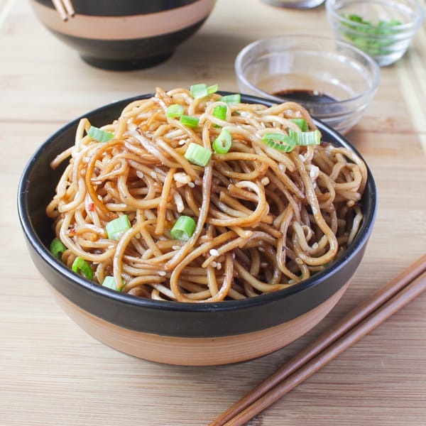 Sesame Noodles with Honey Ginger Sauce in a black and brown bowl with chopsticks are on the side.