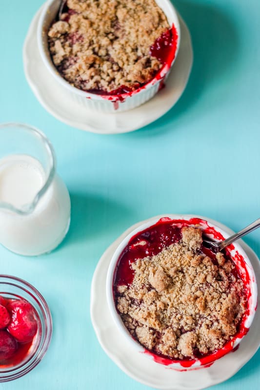 Top down shot of strawberry crumble in white bowls on a blue table top. 