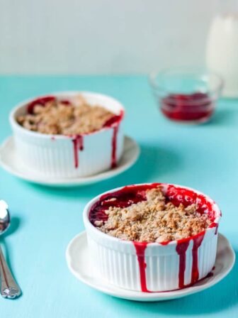Two ramekins with strawberry crumble on a blue table.