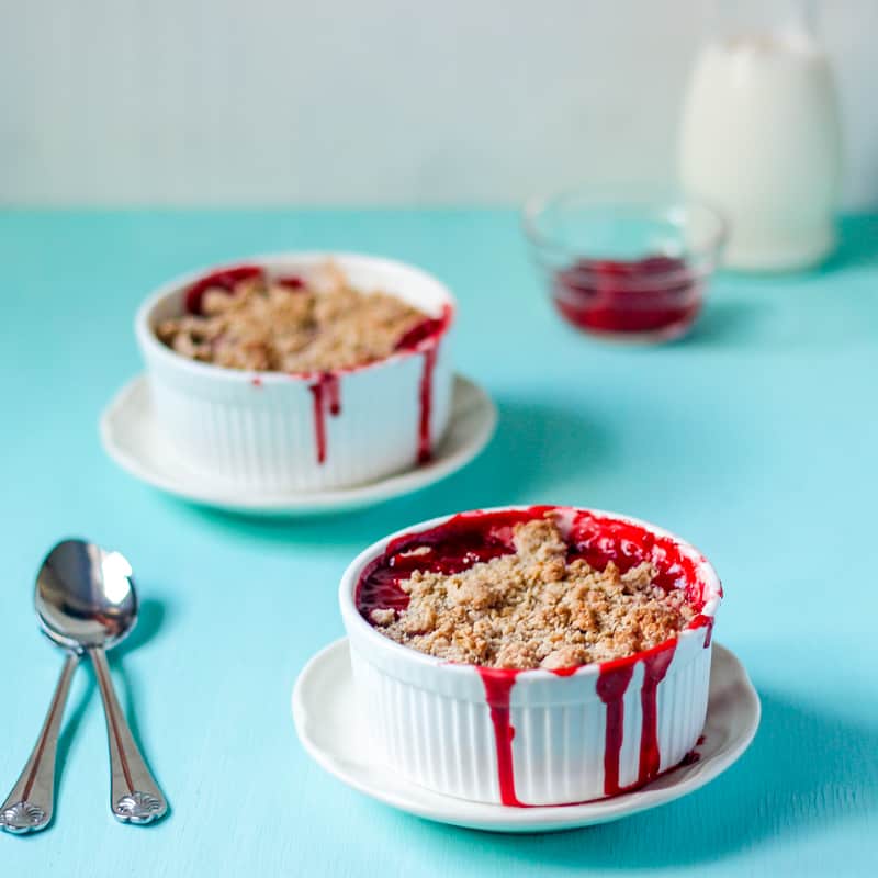 Two ramekins with strawberry crumble on a blue table.