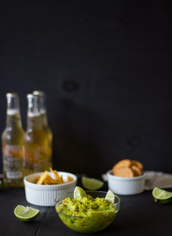 Spicy guacamole in a glass bowl with two bottles of beer in the background. 