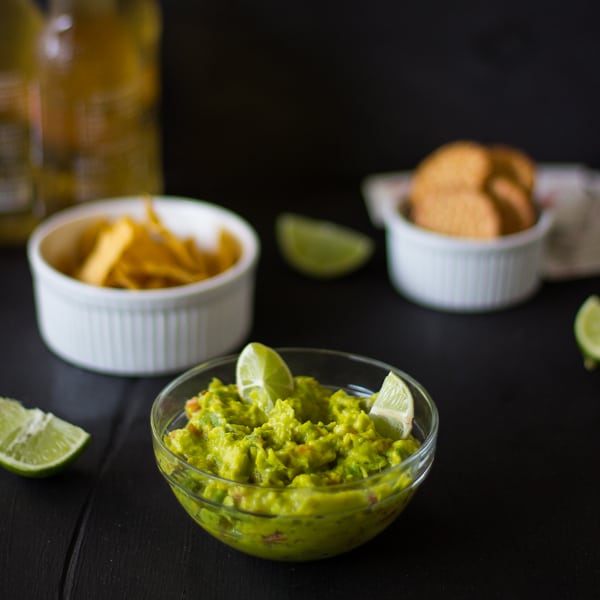 Spicy guacamole in a glass bowl with chips in the background. 