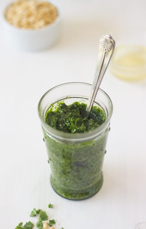 Parsley pesto in a glass bowl with a spoon in it. 