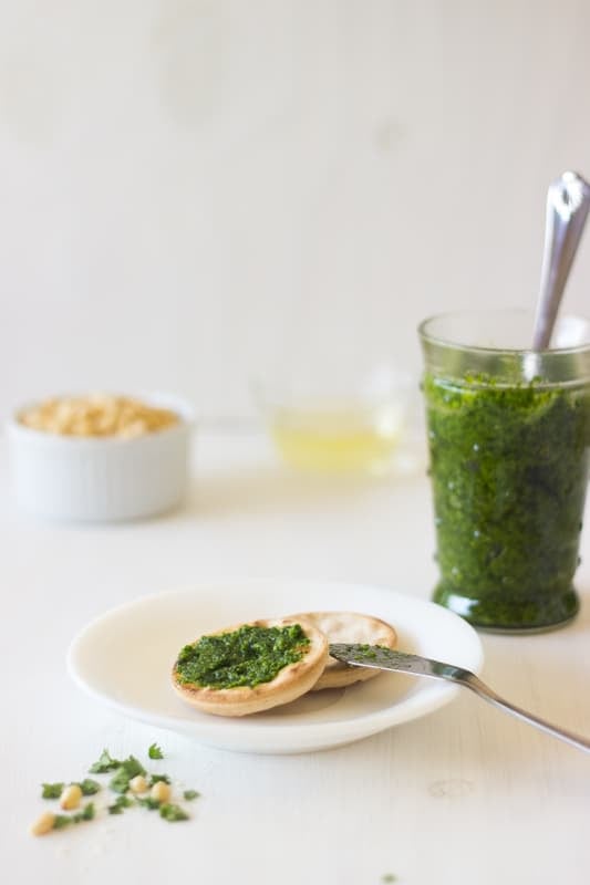 Parsley Pesto spread on a cracker with a jar of pesto in the background.