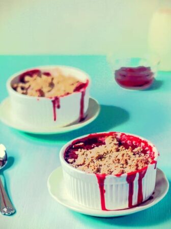 Strawberry crumble in ramekins on a blue table with spoons.