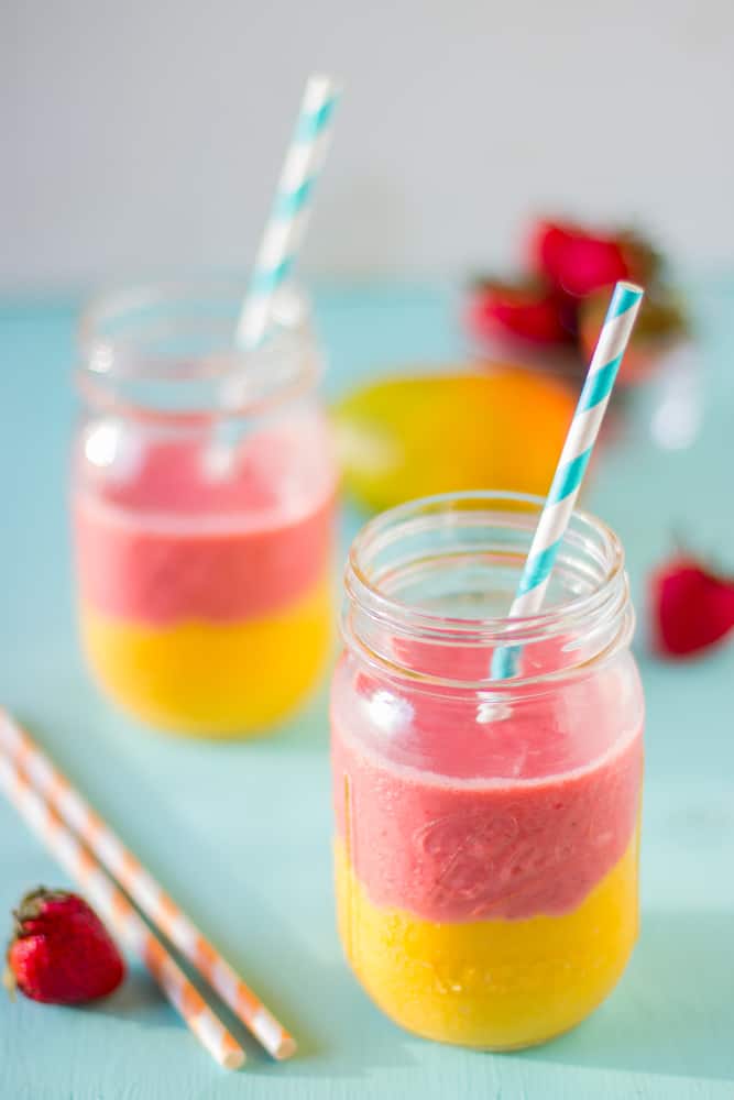 Side shot of two strawberry mango smoothies on a blue table.