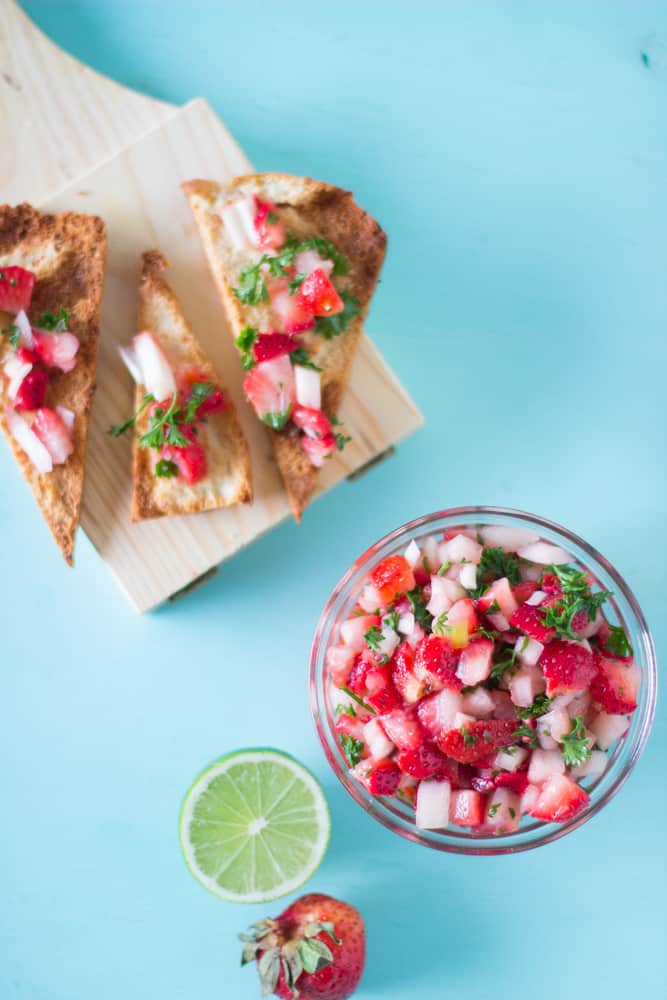 Overhead shot of strawberry salsa in a glass bowl on a blue table. 