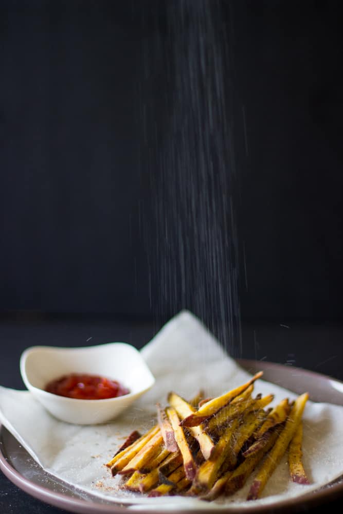 Salt being sprinkled on sweet potato fries.