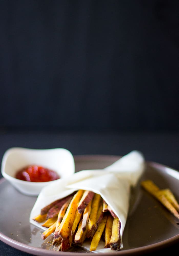 Sweet potato fries wrapped in parchment on a grey plate.