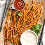 Overhead view of sweet potato fries on pan with bowls of aioli and ketchup