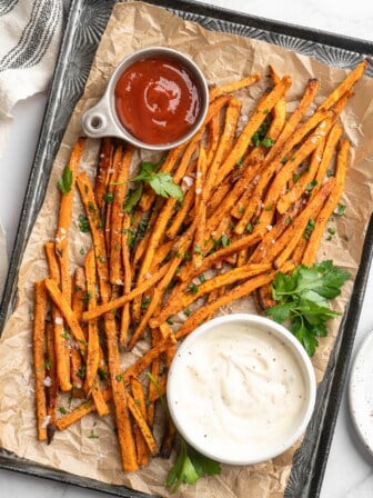 Overhead view of sweet potato fries on pan with bowls of aioli and ketchup