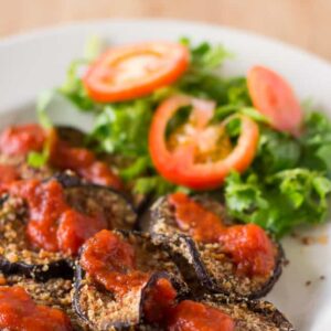 Baked eggplant on a white plate with salad.