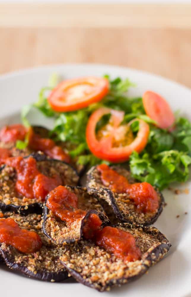 Almond baked eggplant with salad on a white plate.