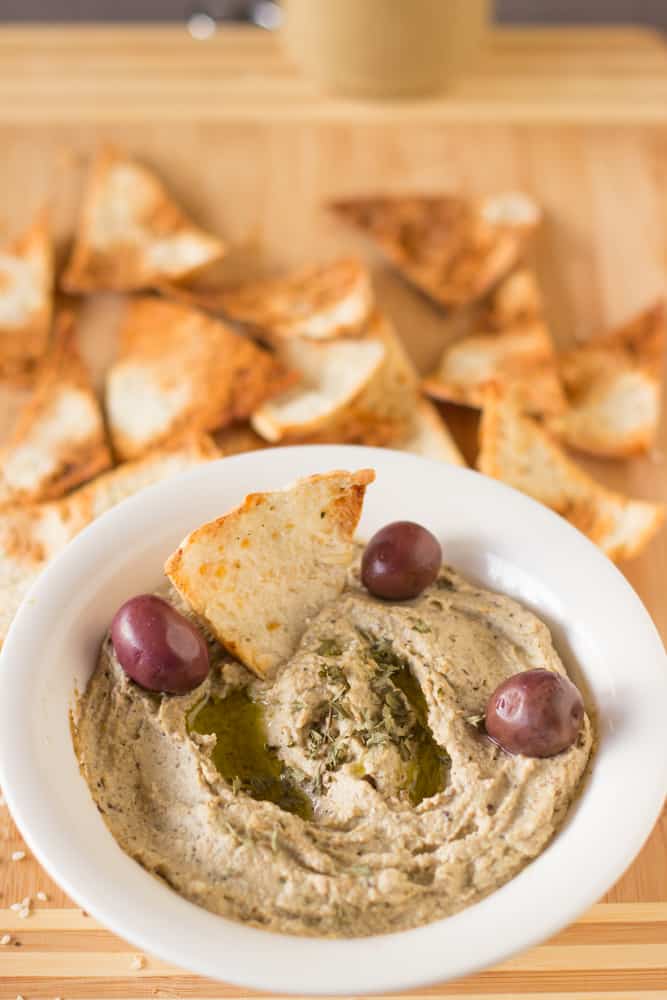 A bowl of baba ganoush with olives and pita chips in it. 