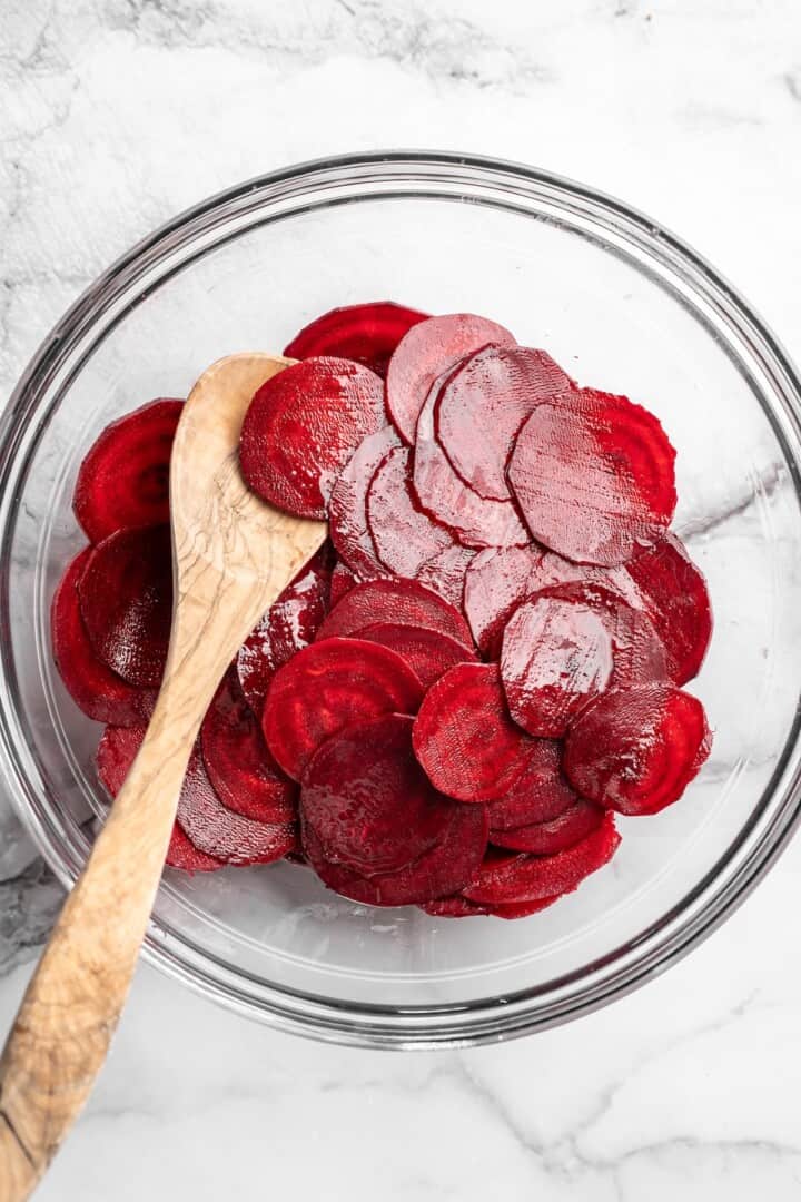 Overhead view of raw beet slices in bowl with wooden spoon