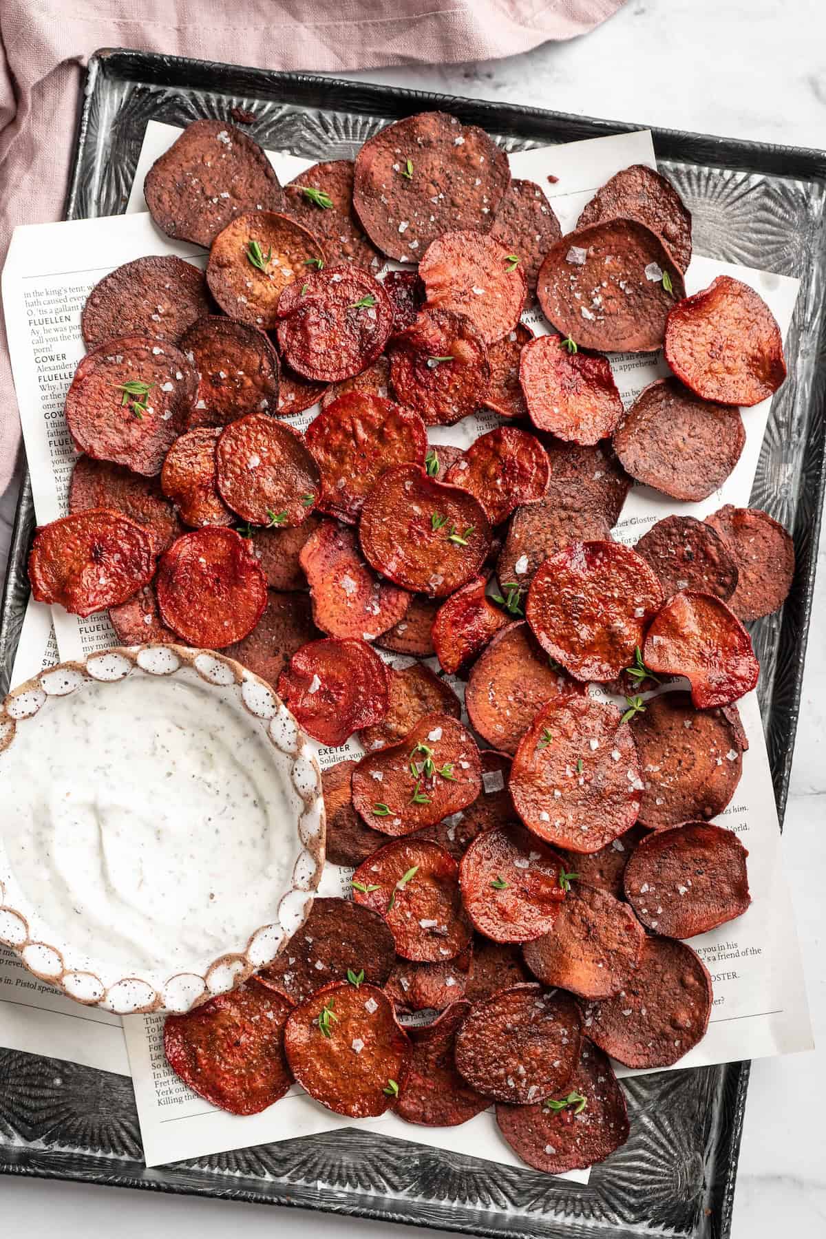 Overhead view of beet chips on sheet pan with bowl of dip