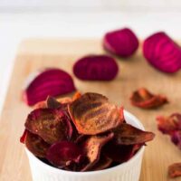 Beet chips in a white ramekin on a wood board.