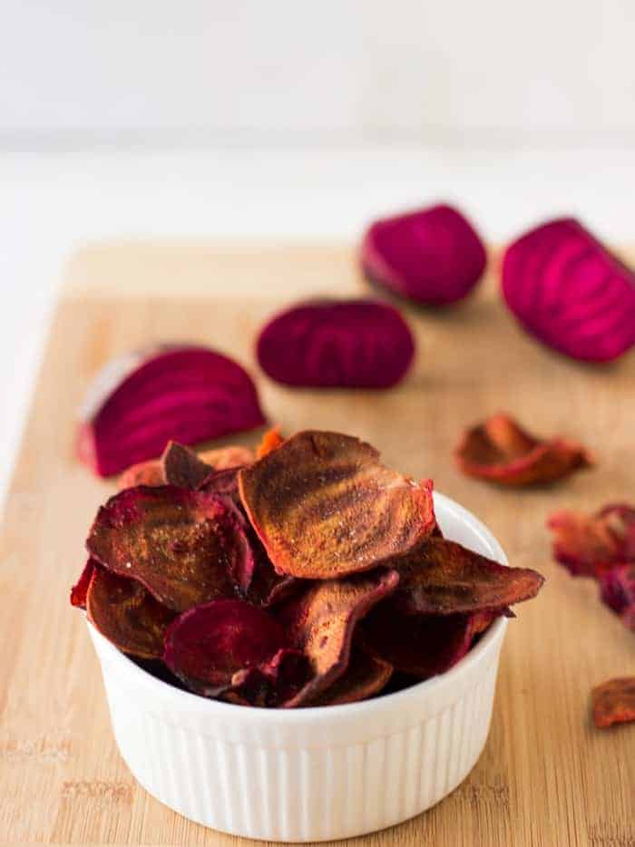 A ramekin of beet chips on a wooden board. 